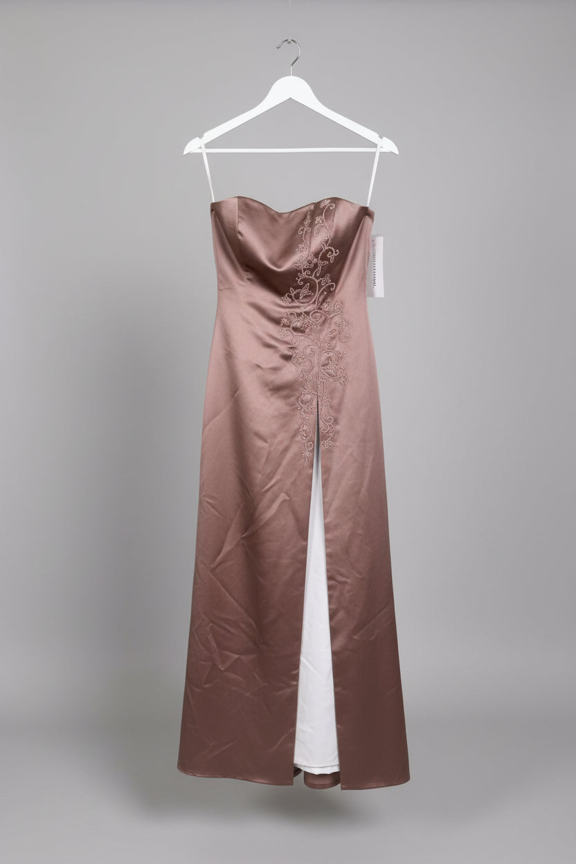 A mauve-brown satin dress with intricate white embroidery hanging on a rack outdoors, with a hand holding the sleeve and grassy ground in the background.