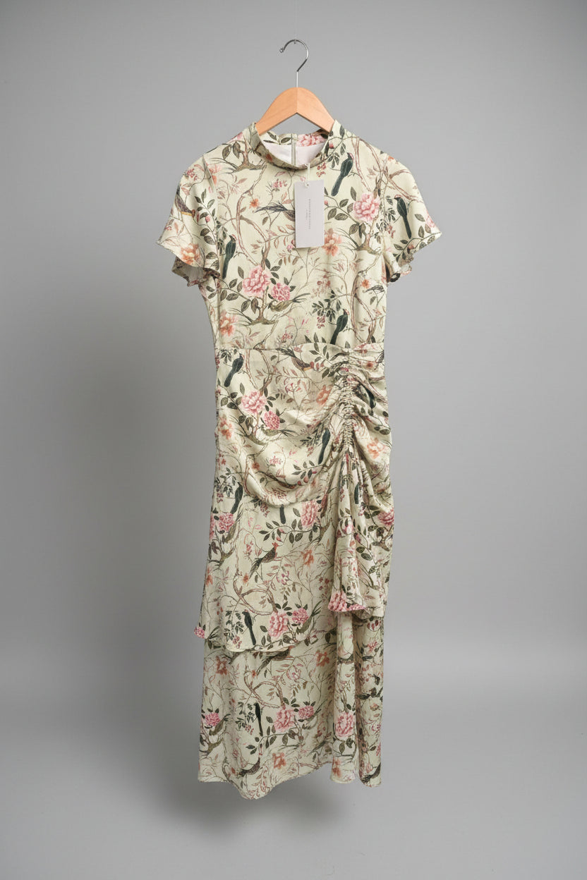 A short-sleeve collared dress with a beige base and pink floral print, hanging on a wooden hanger outdoors next to a metal cart.
