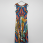 A colorful sleeveless dress with a vibrant geometric and tribal-inspired print in blue, orange, yellow, and green, hanging on a hanger in a retail store setting. 