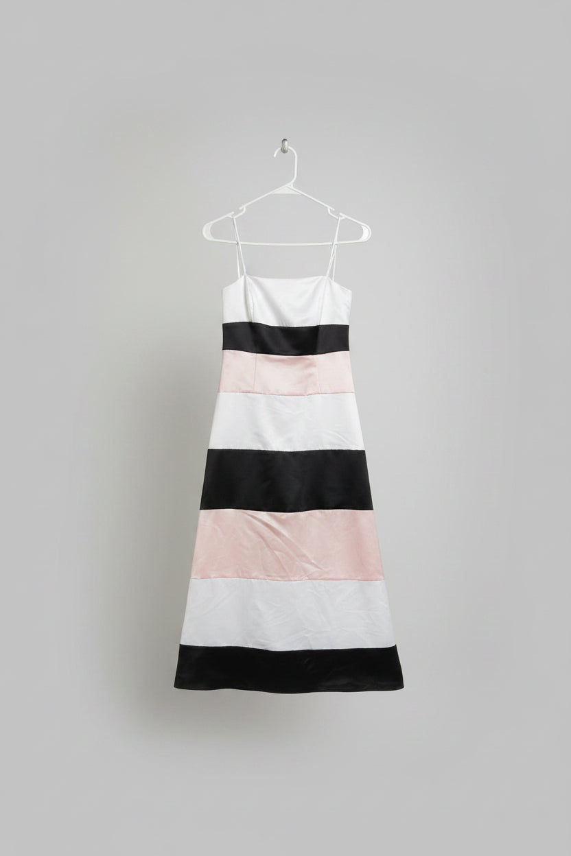 A sleeveless striped dress hanging on a white clothesline outdoors on a metal rack, with grass and a house visible in the background. The dress has wide horizontal stripes in white, black, and light pink.