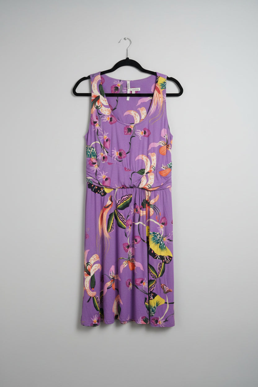 A sleeveless purple dress with a colorful butterfly and floral print, hanging on a black hanger in front of a white door.