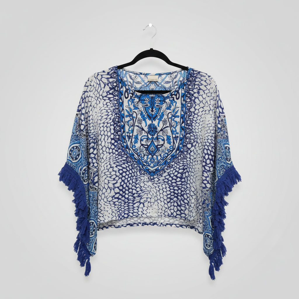 A blue and white patterned fringed poncho or cape hanging on a black rack in a retail store, with a wood floor background.