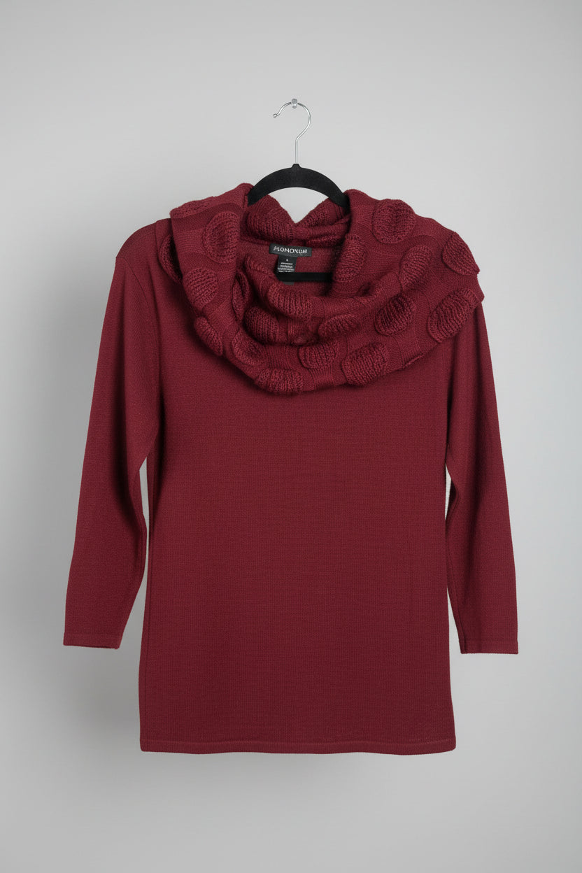 A dark red knit sweater with a chunky, textured cowl neck featuring raised circular details, hanging on a black hanger on a clothing rack.