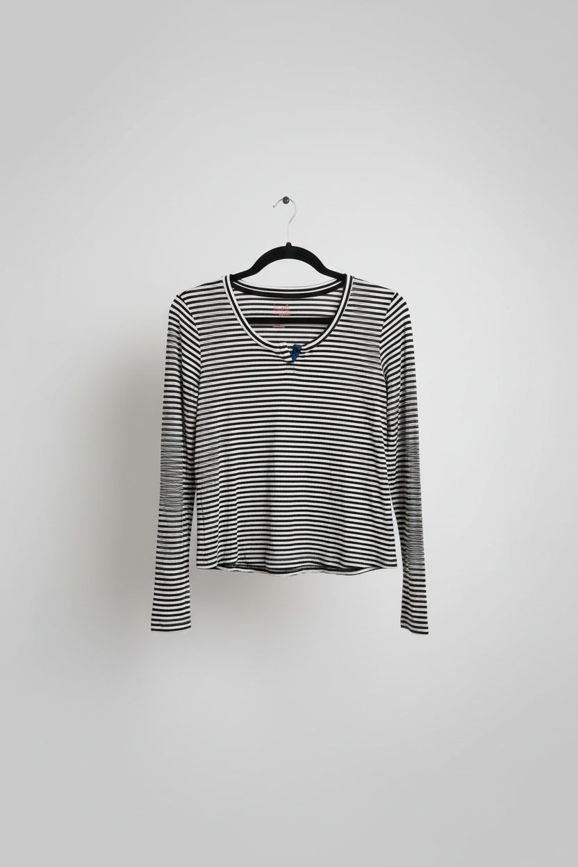 A black and white horizontally striped long-sleeve crop top with a scoop neckline, hanging on a black hanger on a clothing rack.