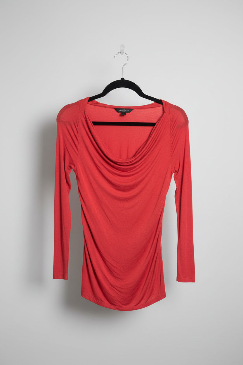 A coral red long-sleeve draped top with side cutouts, hanging on a black hanger on a clothing rack alongside other garments in a retail store.
