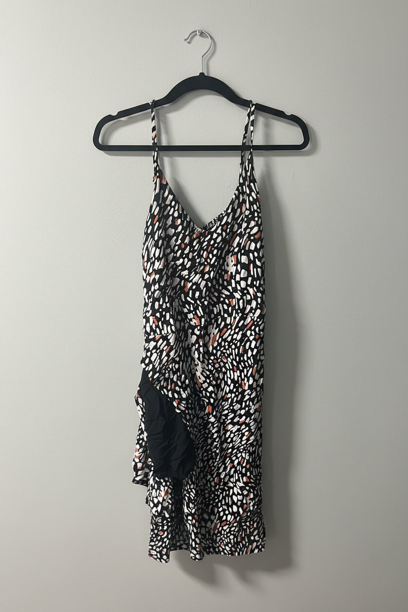 A sleeveless black, white, and orange abstract patterned dress hanging on a black hanger against a plain wall.